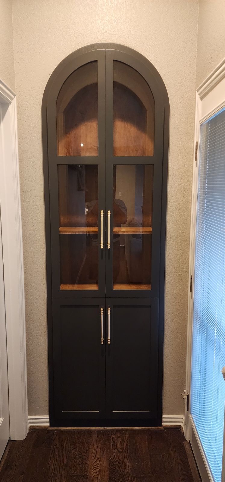 Bespoke arched built-in display cabinet with a black frame, glass doors, and brass pulls