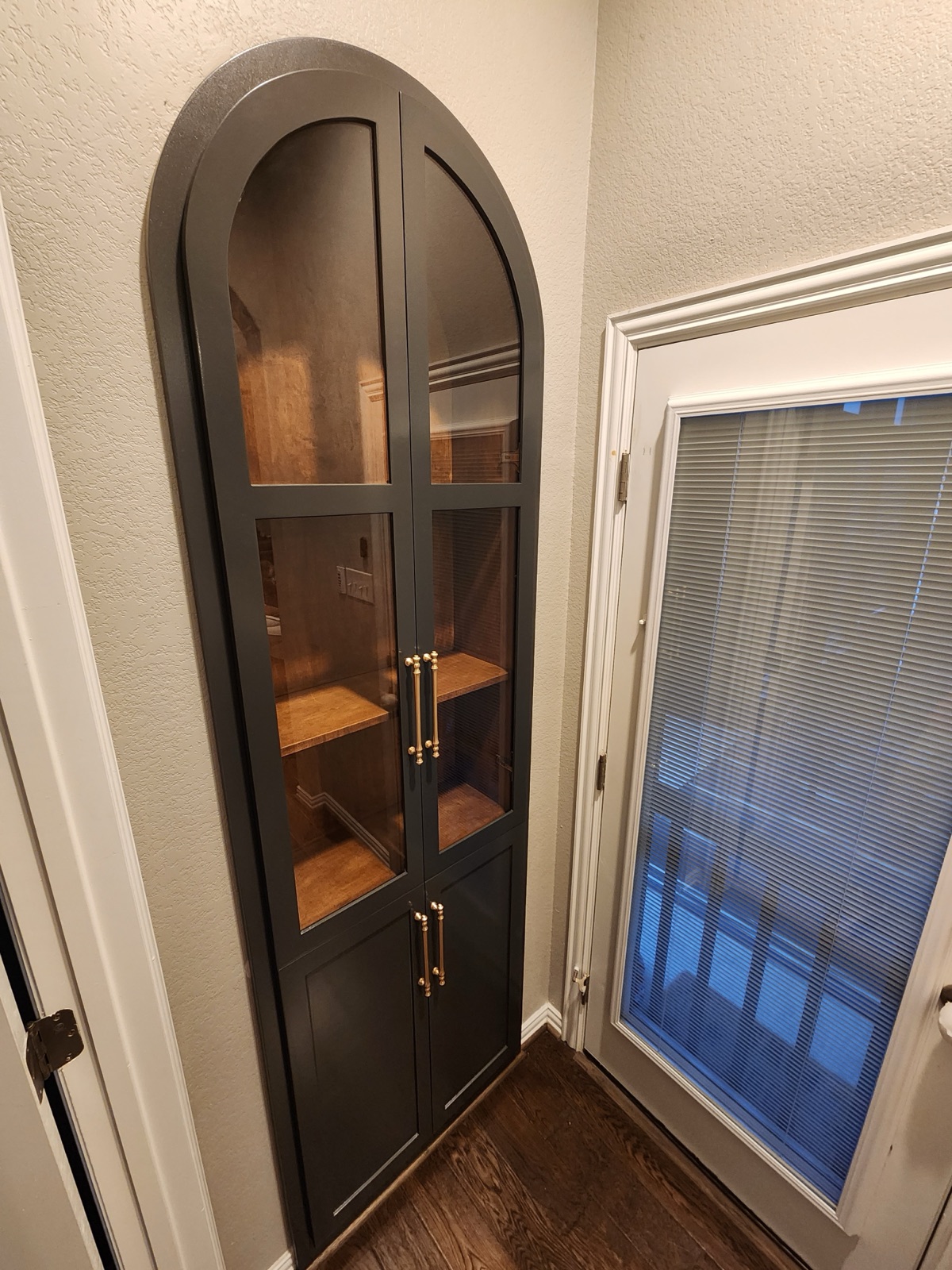 Custom arched built-in cabinet with glass-front doors and brass hardware