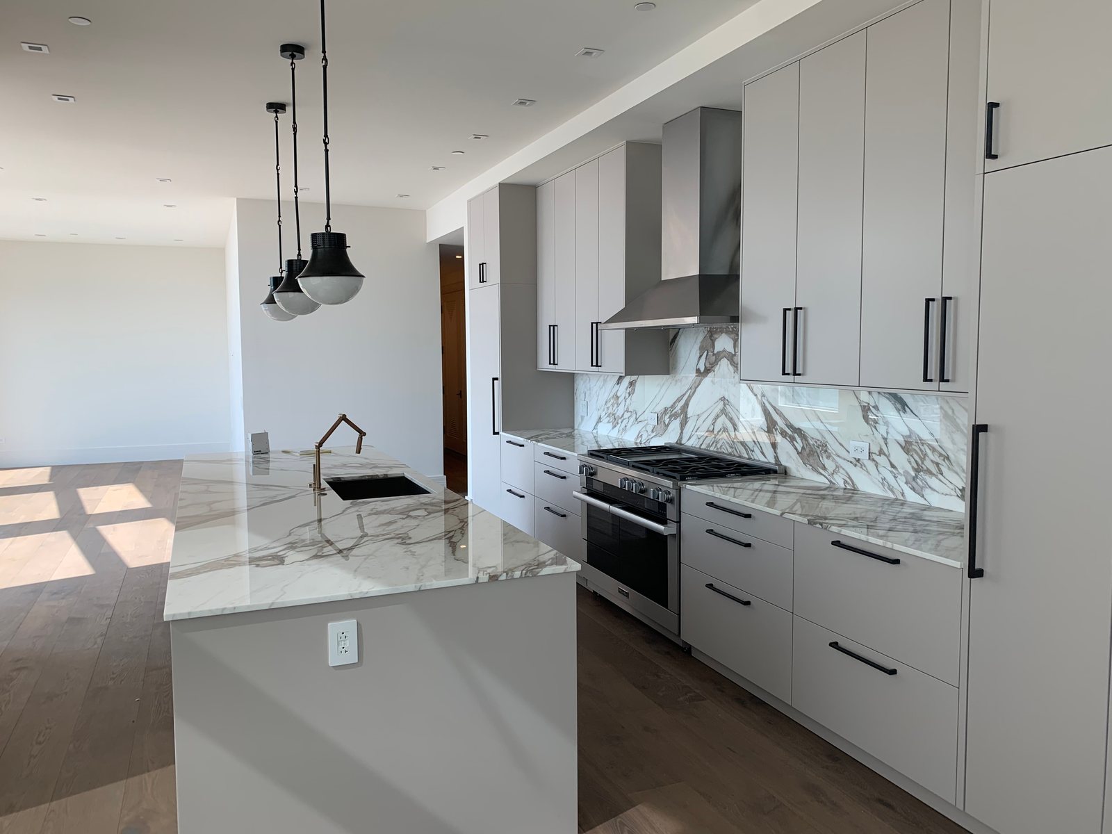 Tailored kitchen with full-height cabinetry, vent hood, and marble-look backsplash